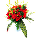 20 red roses arranged in a clear glass vase, gathered with green grasses. This i...